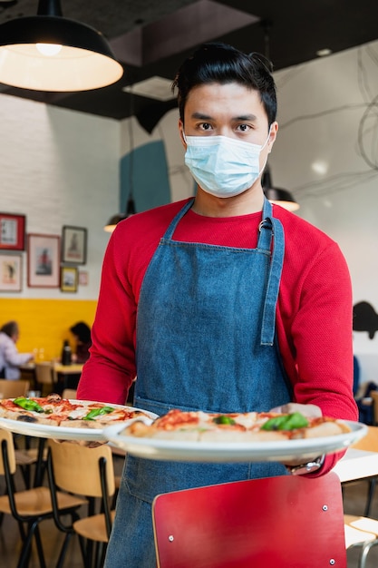 Retrato vertical de garçom asiático com máscara facial protetora servindo pizza
