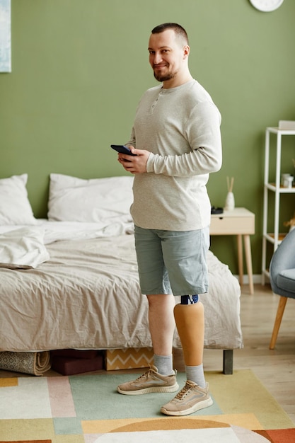 Retrato vertical de homem adulto sorridente com perna protética em pé no interior de casa e segurando sma