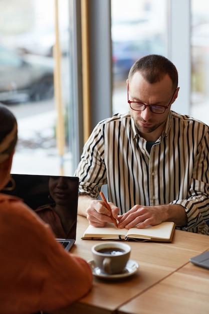 Retrato vertical de homem adulto tomando notas e escrevendo durante uma reunião de negócios na mesa do café