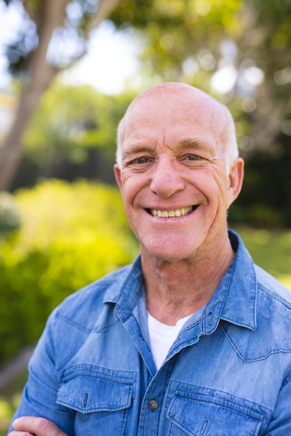 Retrato vertical de homens caucasianos sênior vestindo camisa azul e de pé no jardim