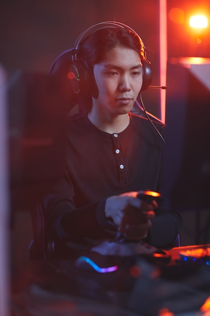 Retrato vertical de jovem asiático jogando videogame usando o turno de corrida no interior escuro do cyber