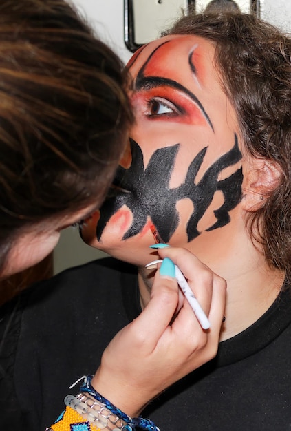 retrato vertical de maquiador profissional fazendo maquiagem e pintando o rosto de uma garota para fantasia de Halloween