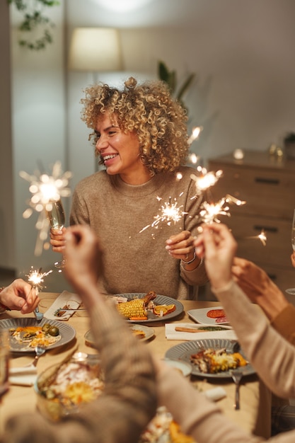 Retrato vertical de mulher mestiça despreocupada segurando estrelinhas enquanto desfruta de um jantar e festa com amigos e familiares