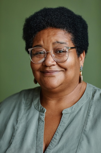 Foto retrato vertical de mulher negra sênior usando óculos e sorrindo para a câmera enquanto posava contra fundo verde