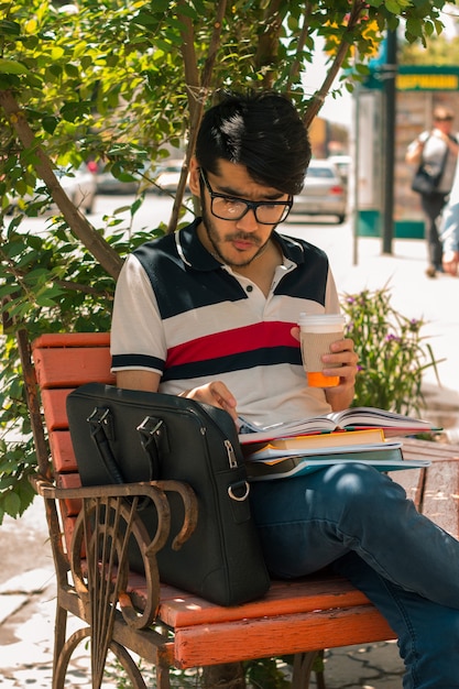 Retrato vertical de um cara lindo e glamouroso de óculos com um livro e uma xícara de café na mão