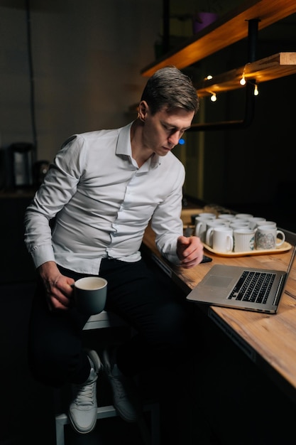 Retrato vertical de um homem concentrado lendo em um laptop trabalhando no prazo durante o turno de trabalho tardio