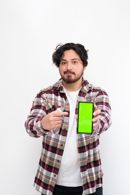 Retrato vertical de um homem segurando o telefone celular com chroma key enquanto aponta para ele em fundo branco