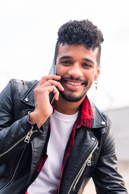 Retrato vertical de um jovem latino sorrindo feliz enquanto fala ao telefone, conceito de tecnologia e estilo de vida urbano