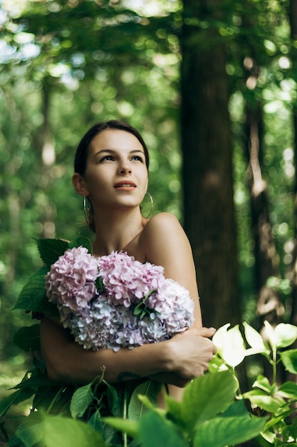 Retrato vertical de uma bela jovem posando no parque com flores em flor Hortênsia