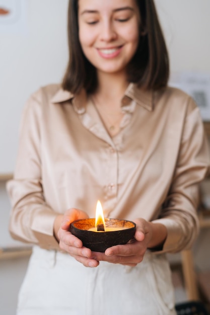 Retrato vertical de uma jovem alegre segurando vela artesanal perfumada queimada nas palmas das mãos Conceito de bem-estar e relaxamento