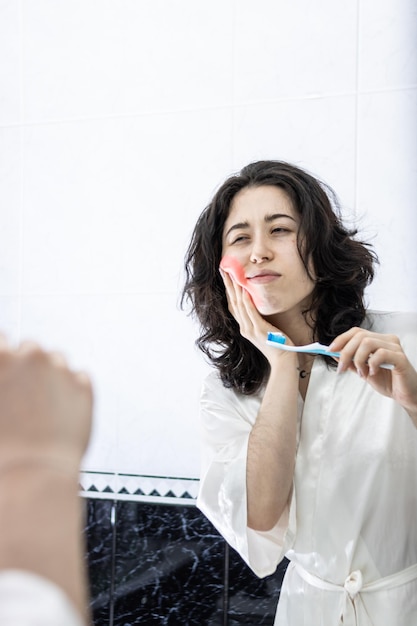 Retrato vertical de uma jovem americana que sofre de dor de dente e dor nas gengivas enquanto escova os dentes no espaço de cópia matinal