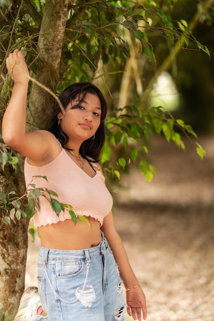 Retrato vertical de uma jovem latina em roupas de verão posando ao lado de algumas árvores