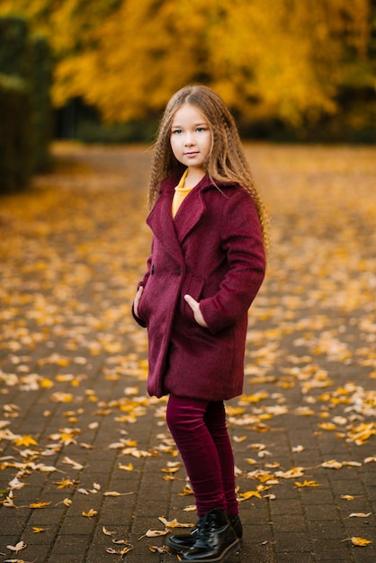Retrato vertical de uma menina encantadora e bonita em um casaco caminhando ao ar livre em um parque ou floresta
