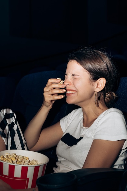 Retrato vertical de uma mulher sentada em uma cadeira em um cinema comendo uma tigela de popcorn