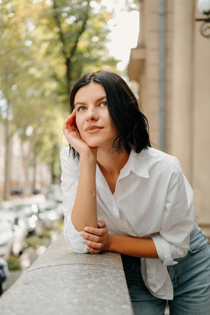 Retrato vertical de uma mulher sonhadora vestindo camisa branca encostada na grade