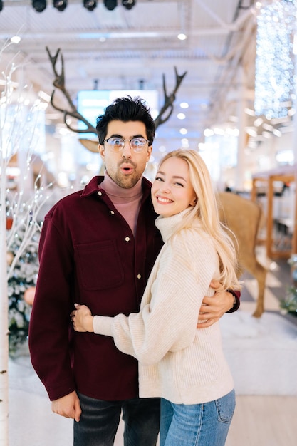 Retrato vertical de engañar a la esposa con el marido con cuernos de ciervo colgando de pie en el salón del centro comercial Celebrar en la víspera de Navidad