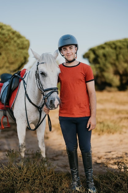 Foto retrato vertical de un estudiante de escuela de equitación posando con su caballo