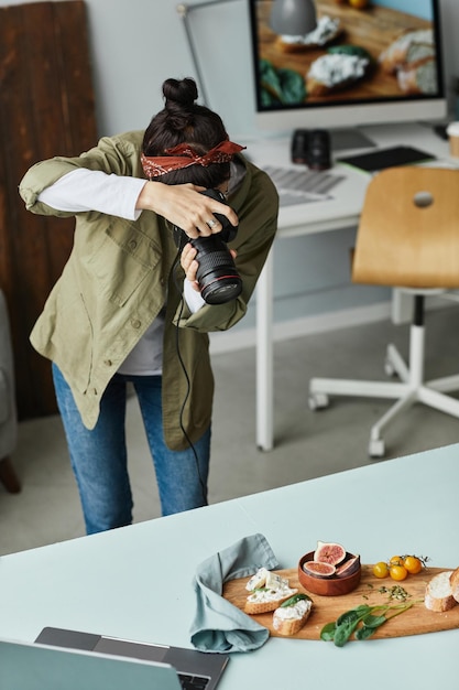 Retrato vertical de una fotógrafa de comida tomando fotos mientras trabaja en un estudio casero