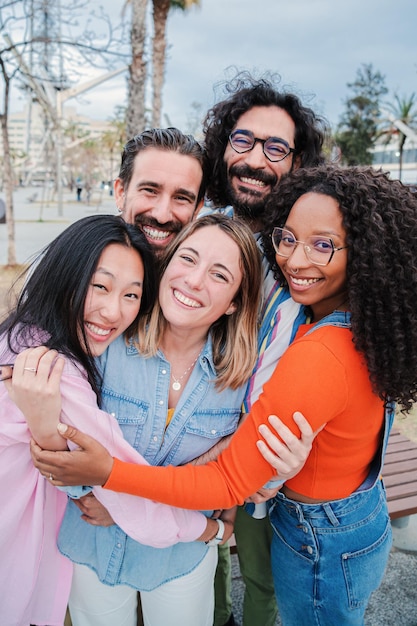 Foto retrato vertical de un grupo de alegres amigos jóvenes adultos abrazándose unos a otros sonriendo felices