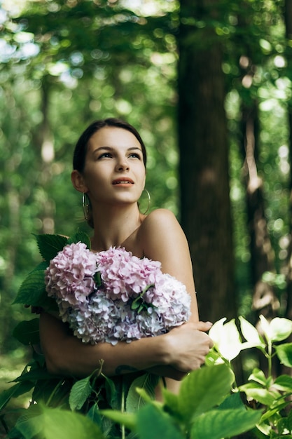 Retrato vertical de una hermosa mujer joven posando en un parque con flores en flor Hortensia