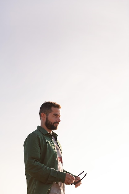 Retrato vertical de un hombre atractivo con gafas de sol en las manos con el cielo en segundo plano concepto de ocio y relax copia espacio para texto