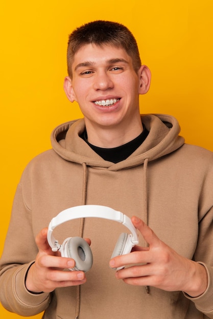 Retrato vertical de un hombre sonriente con capucha sosteniendo auriculares blancos