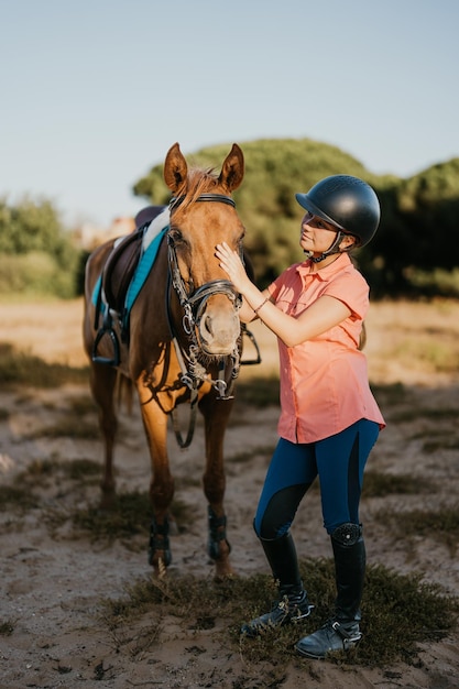 Retrato vertical de una jinete parada junto a su pony acariciando su cabeza