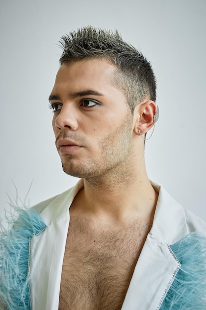 Retrato vertical de un joven gay con maquillaje mirando hacia otro lado contra un blanco