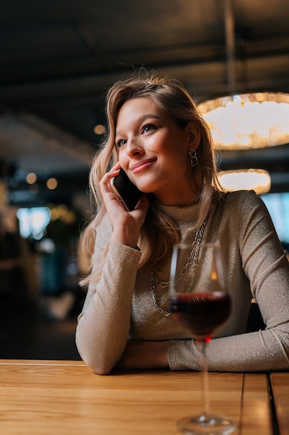 Retrato vertical de una joven positiva y linda hablando por teléfono móvil con un amigo sonriendo discutiendo las últimas noticias disfrutando de una agradable conversación