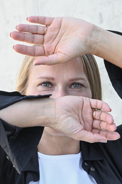 Retrato vertical de una joven rubia con las manos cubriendo la cara y solo muestra el aspecto visible de sus ojos de belleza