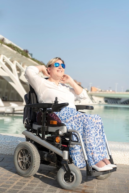 Retrato vertical de una mujer con gafas de sol sentada en una silla de ruedas disfrutando de un día soleado