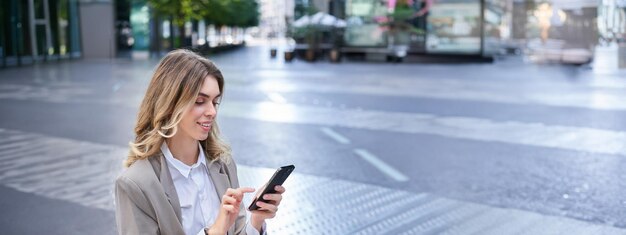 Retrato vertical de una mujer de negocios en traje usando su teléfono relajándose al aire libre sentada en un banco