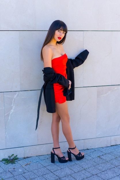 Retrato en vestido rojo en una pared gris chica atractiva posó sonriente y foto vertical