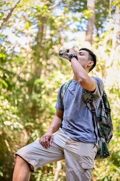 Retrato Viajero asiático cansado y sediento o excursionista bebe agua de una botella mientras descansa