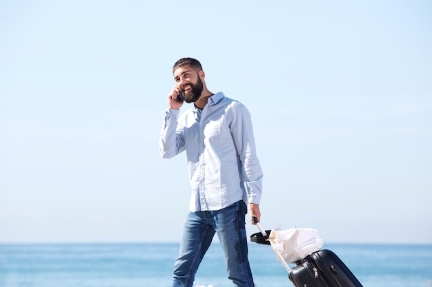 Retrato del viajero feliz que camina por el mar que habla en el teléfono móvil