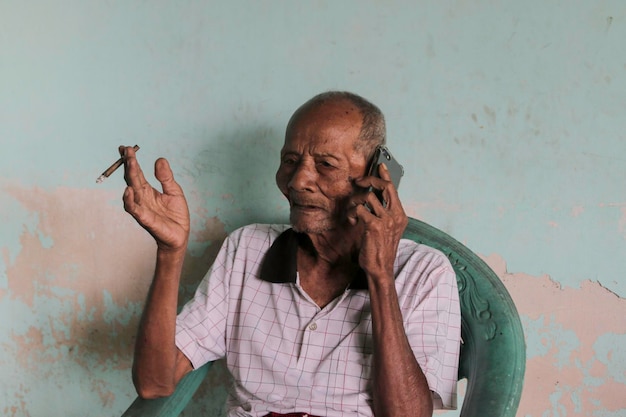 Un retrato del viejo abuelo indonesio llamando en un teléfono inteligente