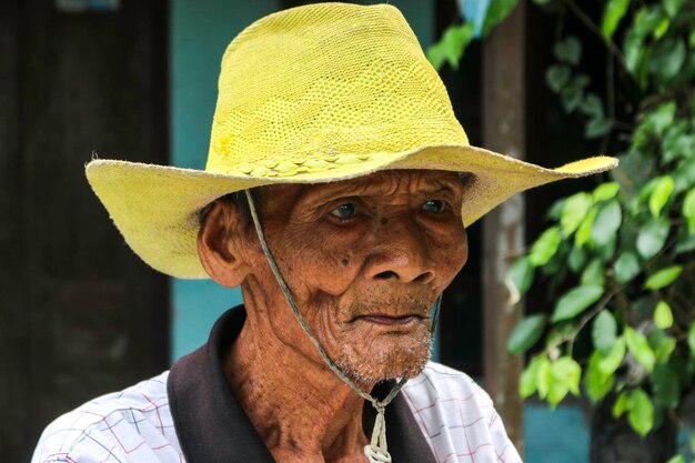 Un retrato de un viejo granjero indonesio usa un sombrero amarillo con una bicicleta vieja