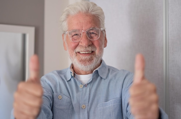 Retrato de un viejo y guapo hombre caucásico de barba con los pulgares hacia arriba mirando a la cámara