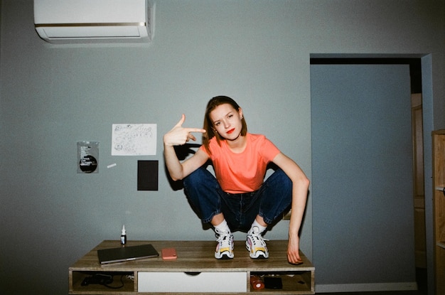 Foto retrato vintage en cámara de película con flash en casa modelo de niña posando en cámara de película sentada en la mesa en el interior foto de 35 mm con grano retrato moderno de 35 mm de modelo atractivo en el interior por la noche