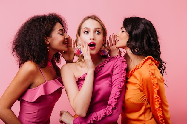 Retrato de vista frontal de una chica rubia sorprendida hablando con amigos Tres señoritas compartiendo rumores