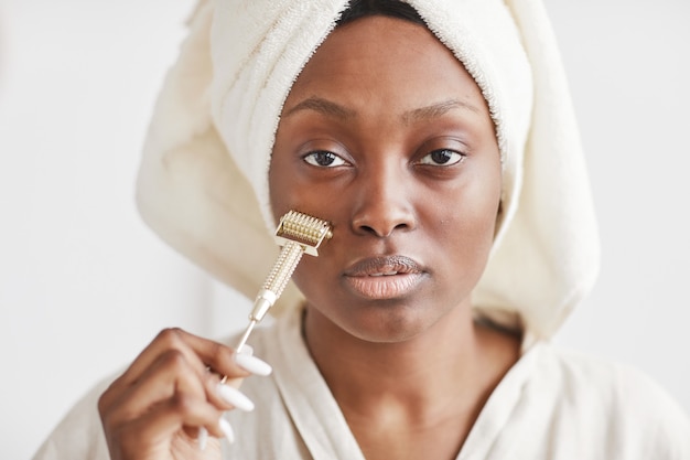 Retrato de vista frontal de hermosa mujer afroamericana haciendo masaje facial microdermal mientras está en casa y mirando a cámara, espacio de copia