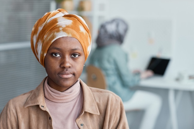 Retrato de vista frontal de la mujer afroamericana moderna con pañuelo en la cabeza en la oficina y mirando a la cámara, espacio de copia