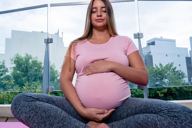 Retrato vista frontal mujer joven en casa sentada meditando tocando su vientre con las manos