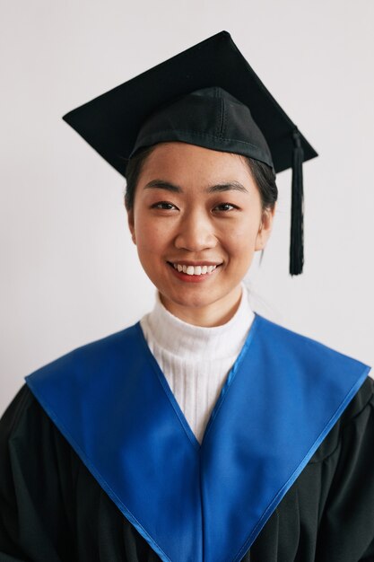 Retrato de vista frontal vertical de la joven mujer asiática vistiendo batas de graduación y sonriendo a la cámara