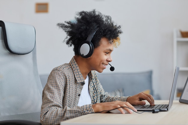 Retrato de vista lateral de un adolescente afroamericano jugando videojuegos en casa y sonriendo con alegría, joven jugador o concepto de blogger, espacio de copia