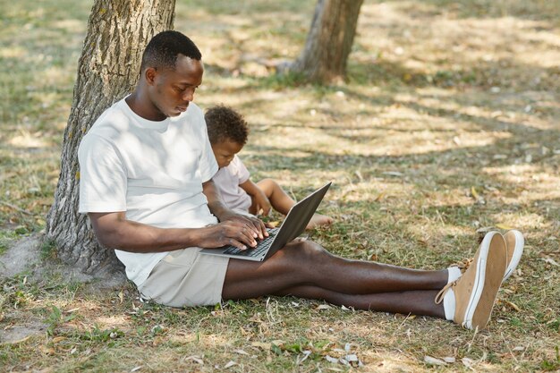 Retrato De Vista Lateral De Cuerpo Entero De Hombre Joven Africano Americano Que Usa La Computadora Portátil Al Aire Libre En El Parque Con Lindo ...