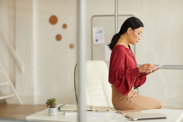 Retrato de vista lateral de la elegante empresaria asiática sentada en el escritorio y con tableta digital en la moderna oficina blanca, espacio de copia
