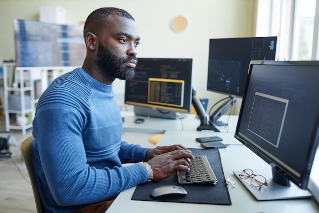 Retrato de vista lateral del hombre afroamericano como programador de computadoras escribiendo código en el lugar de trabajo de la oficina