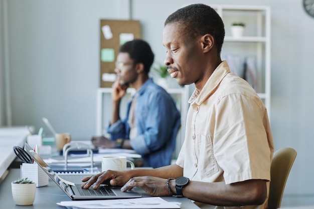 Retrato de vista lateral de un hombre negro adulto que usa una computadora mientras trabaja en la oficina o en el espacio de coworking