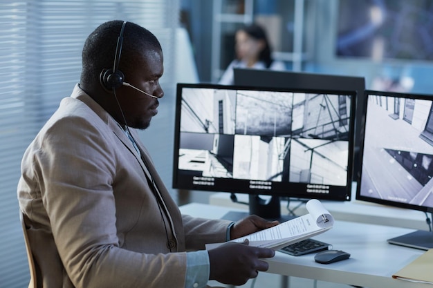 Retrato de vista lateral de un hombre negro con auriculares mientras ve la transmisión de vigilancia en la pantalla en securi